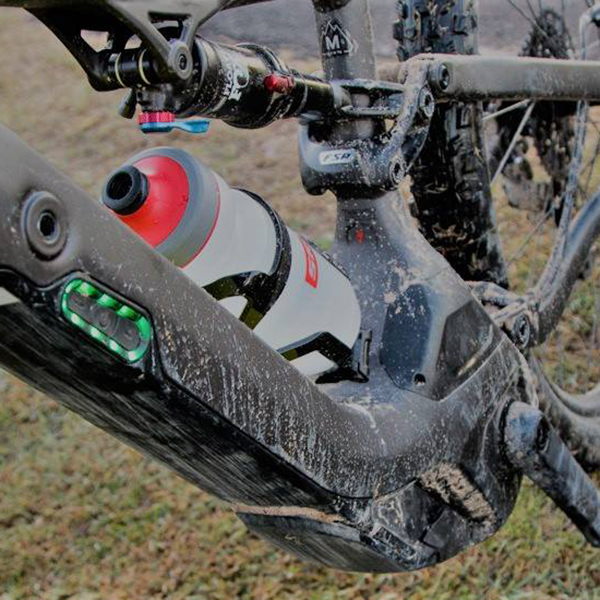Close-up of a mud-covered full-suspension mountain bike frame and drink bottle